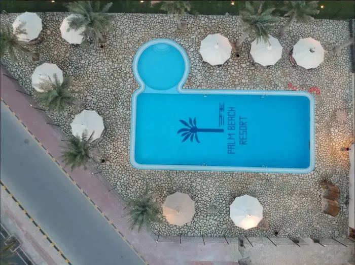 مسبح منتجع شاطئ النخيل من الأعلى تحيط به المظلّات والنخيل